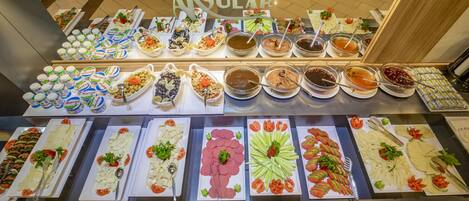 Un bufé con diversos alimentos, entre ellos ensaladas, carnes y salsas, dispuesto sobre una mesa.