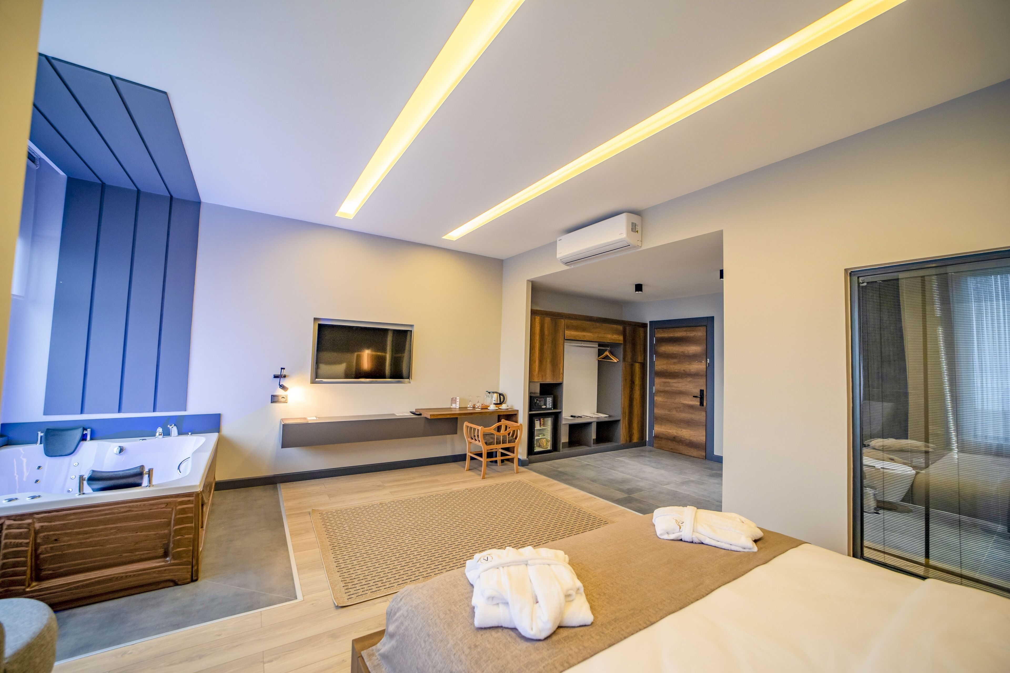 A modern hotel room with a large bathtub, a bed, a desk, and a wardrobe.
