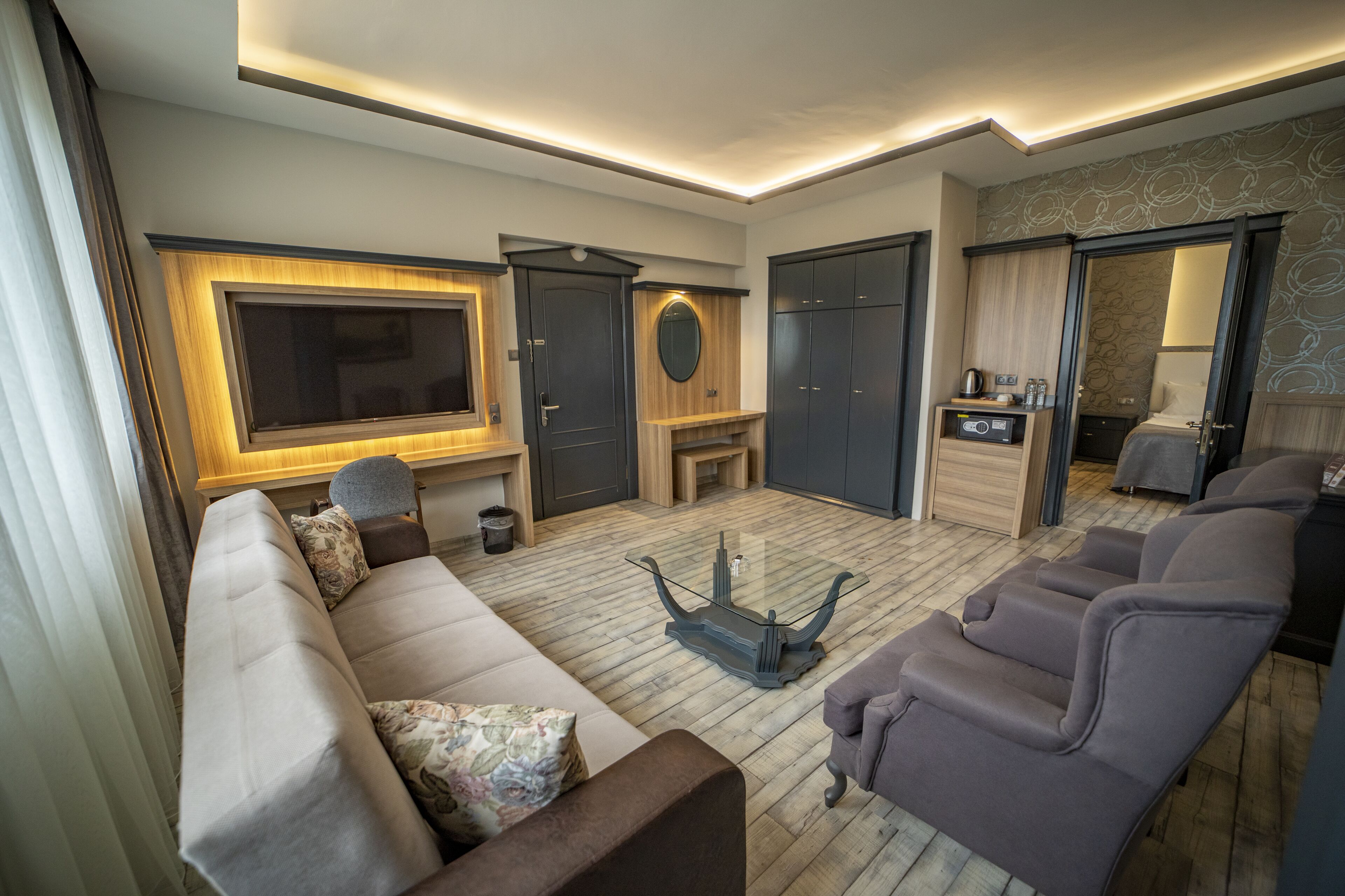 Una habitación de hotel moderna con una televisión de pantalla plana grande, un sofá, un sillón reclinable, una mesa de centro y un armario.