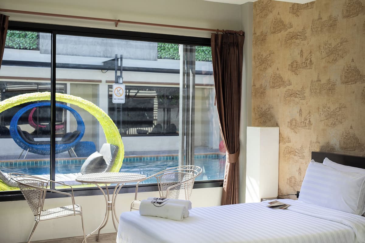 Habitación de hotel con cama, ventana con vista a una piscina y un cartel de 'No estacionar', además de un papel tapiz estampado.