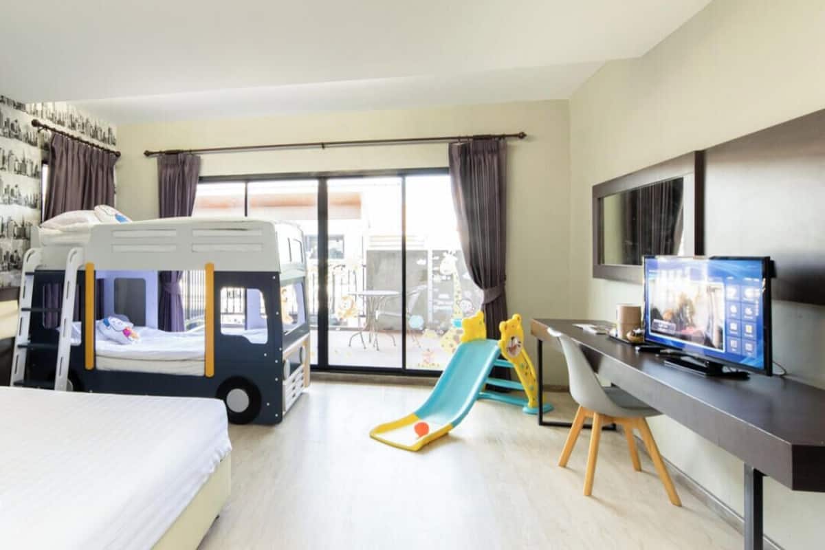 Habitación de hotel con literas, un escritorio con computadora, televisión y un ventanal con cortinas.
