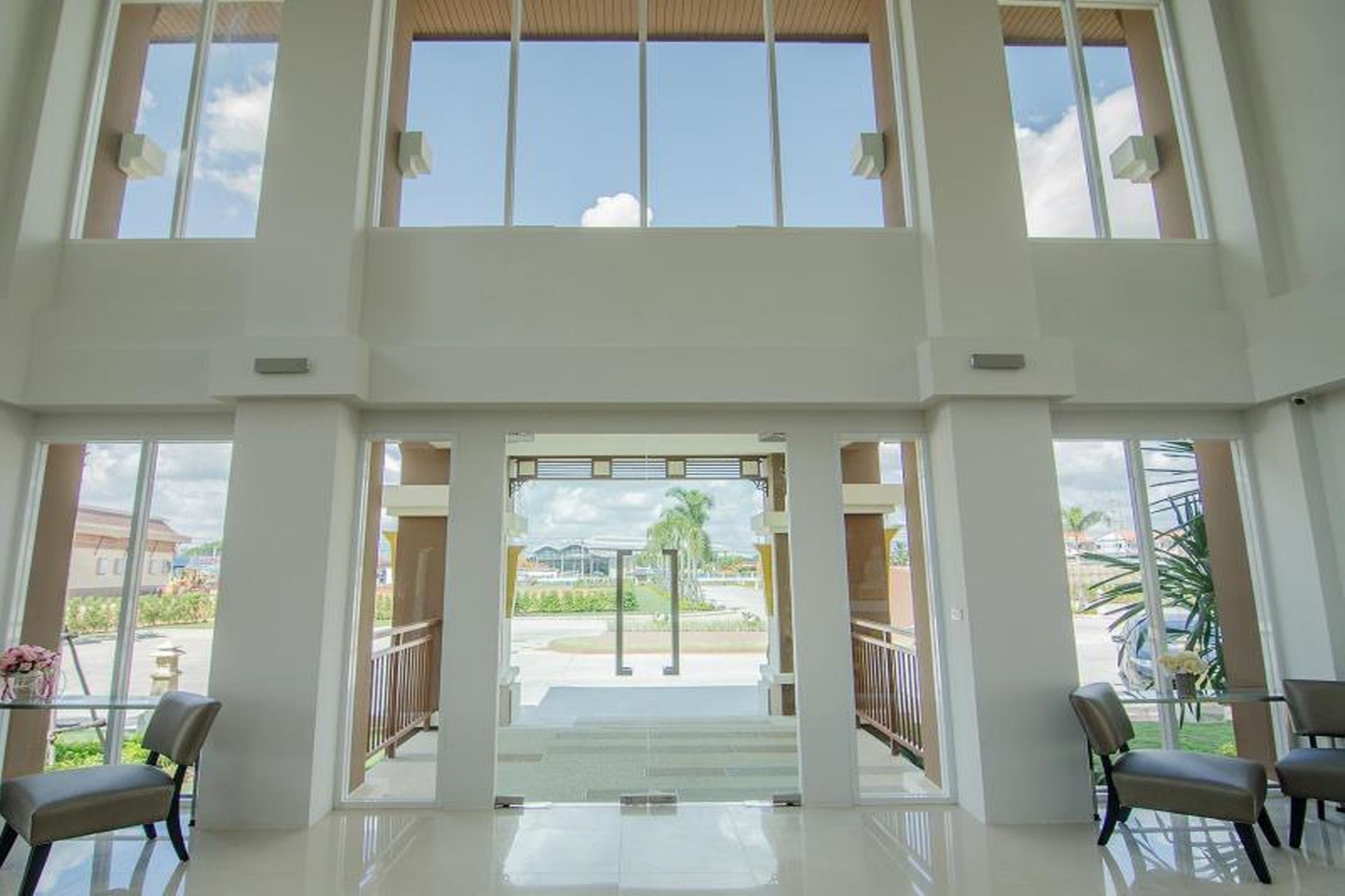 A spacious lobby with high ceilings and large windows, leading to an outdoor area with a palm tree and a view of a parking lot.