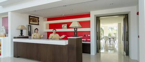 Un mostrador de recepción con dos empleados, una pared de acento roja y vistas al área exterior.