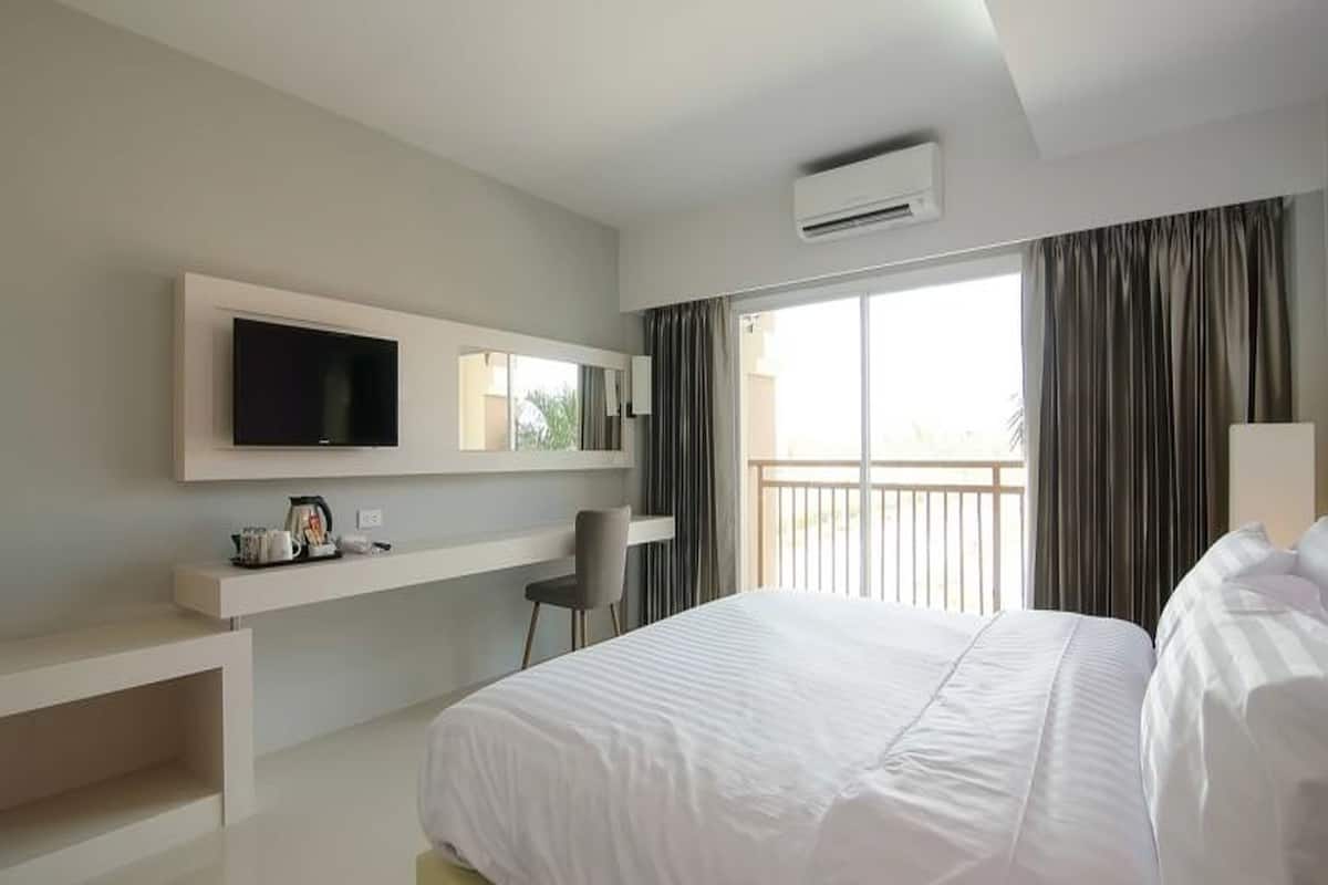 Habitación de hotel con una cama grande, televisión montada en la pared, escritorio con silla y balcón con cortinas.