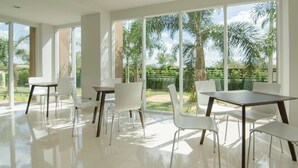 A spacious dining area with large windows, white chairs, and a central table. - The Lake Hotel (Khon Kaen)