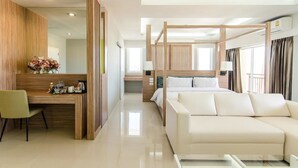 A modern hotel room with a wooden desk, a green chair, a white sofa, and a large bed with a canopy. - The Lake Hotel (Khon Kaen)