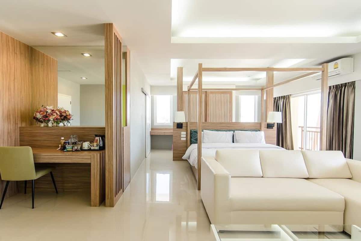 Una habitación de hotel moderna con un escritorio de madera, una silla verde, un sofá blanco y una cama grande con dosel.