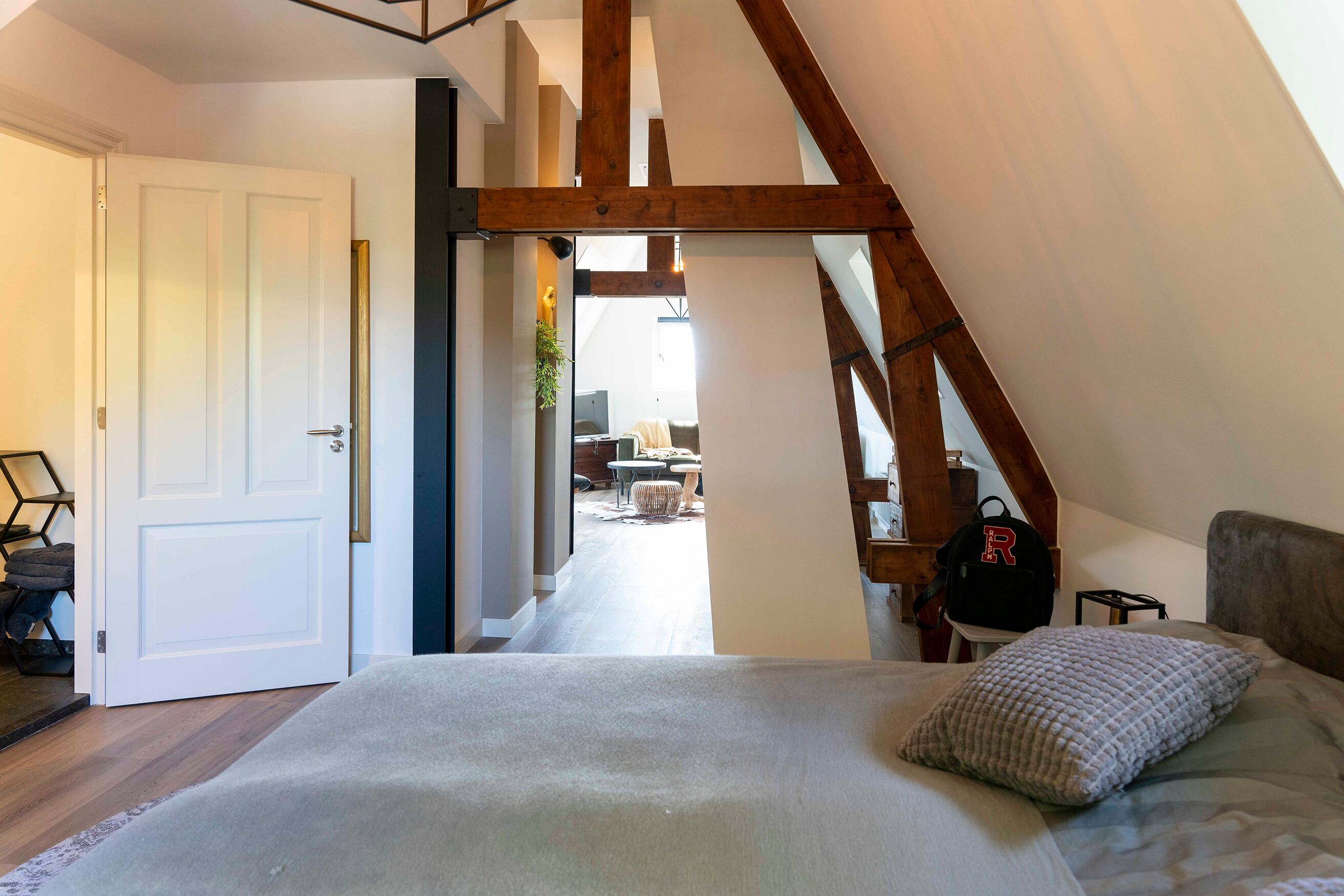 Een slaapkamer met een groot bed, een houten balk in het plafond en uitzicht op de zithoek.