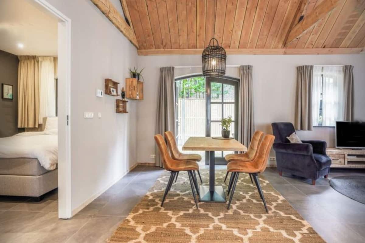A modern living room with a wooden ceiling, a dining area with two chairs and a table, a sofa, and a TV.