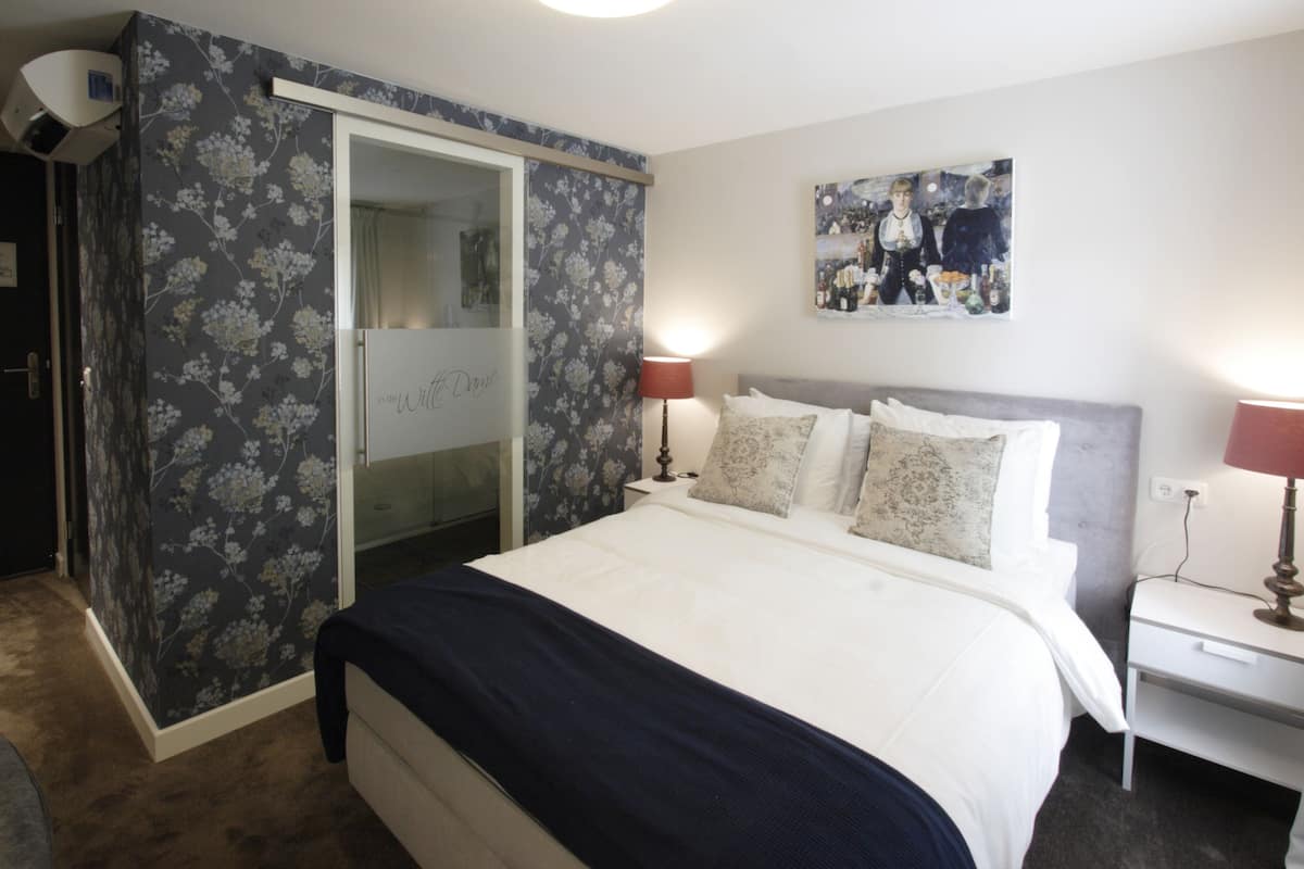A bedroom with a bed, nightstands, a mirror, and a painting on the wall.