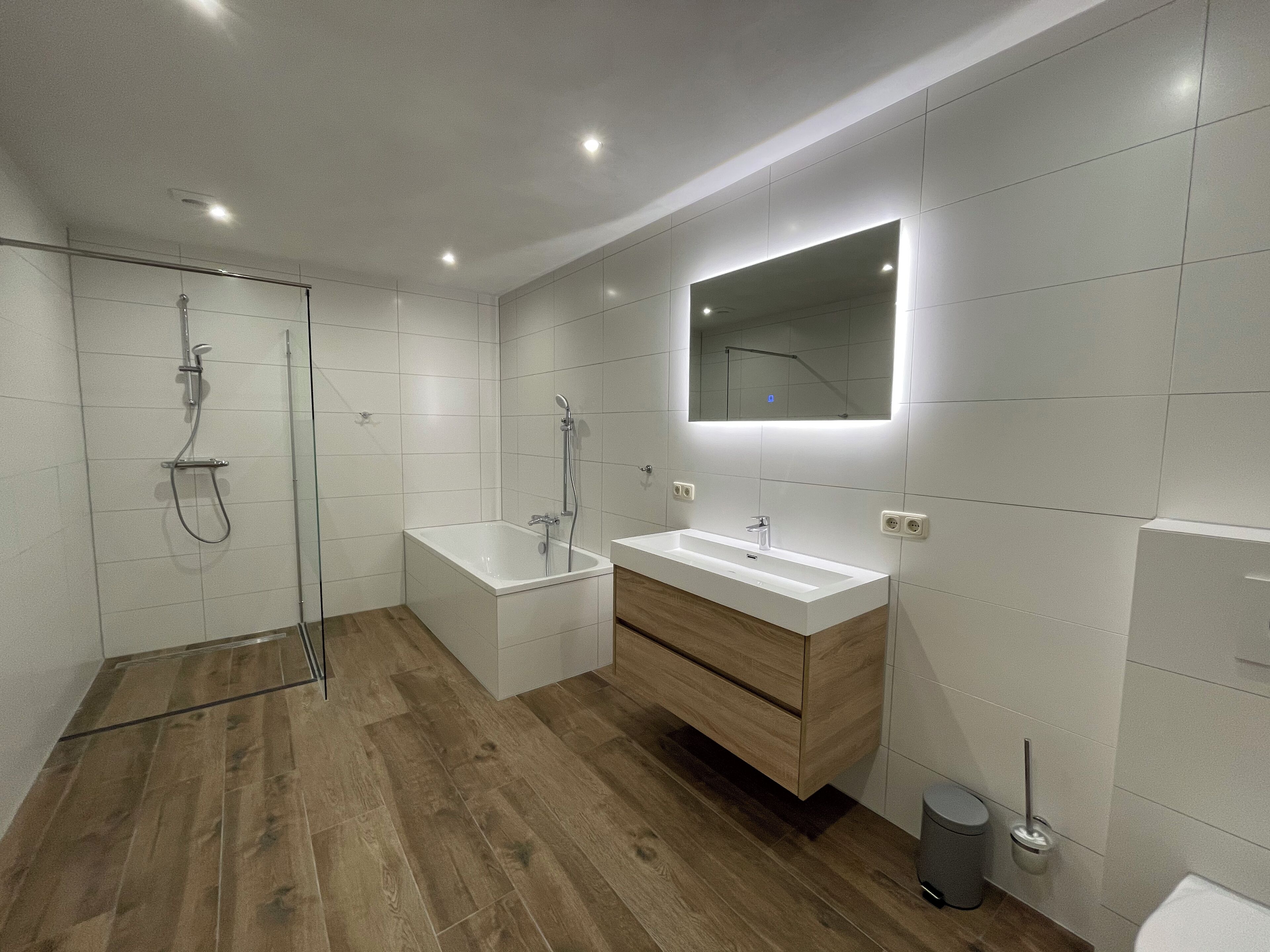 Un baño moderno con suelo de madera, una bañera grande, un tocador con espejo y una zona de ducha.