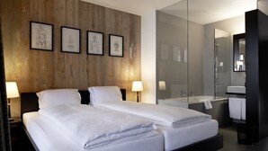 Una habitación de hotel moderna con una pared de madera, dos camas, un espejo grande y un baño con bañera y lavamanos.
