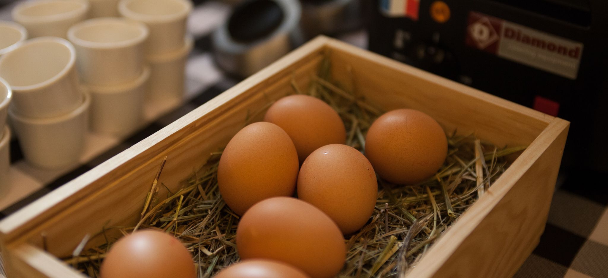 Una cassa di legno contenente sei uova marroni, posata su una tovaglia a quadri.