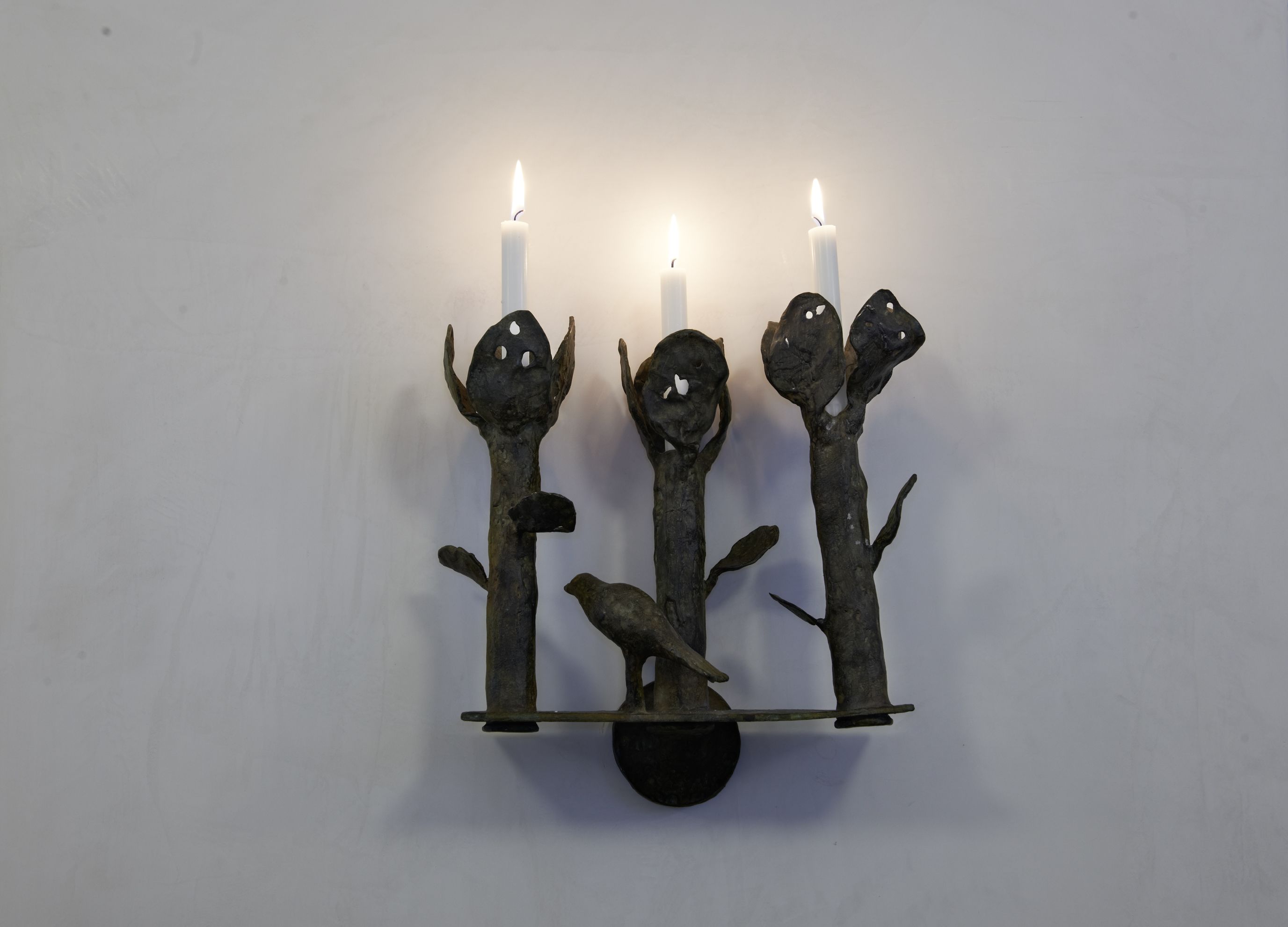 Un candelabro de pared con tres velas y una escultura de pájaro.