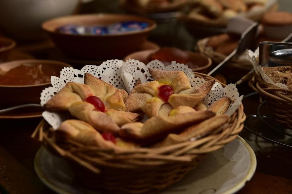 A basket of bread rolls with a cherry on top, placed on a table with other food items.