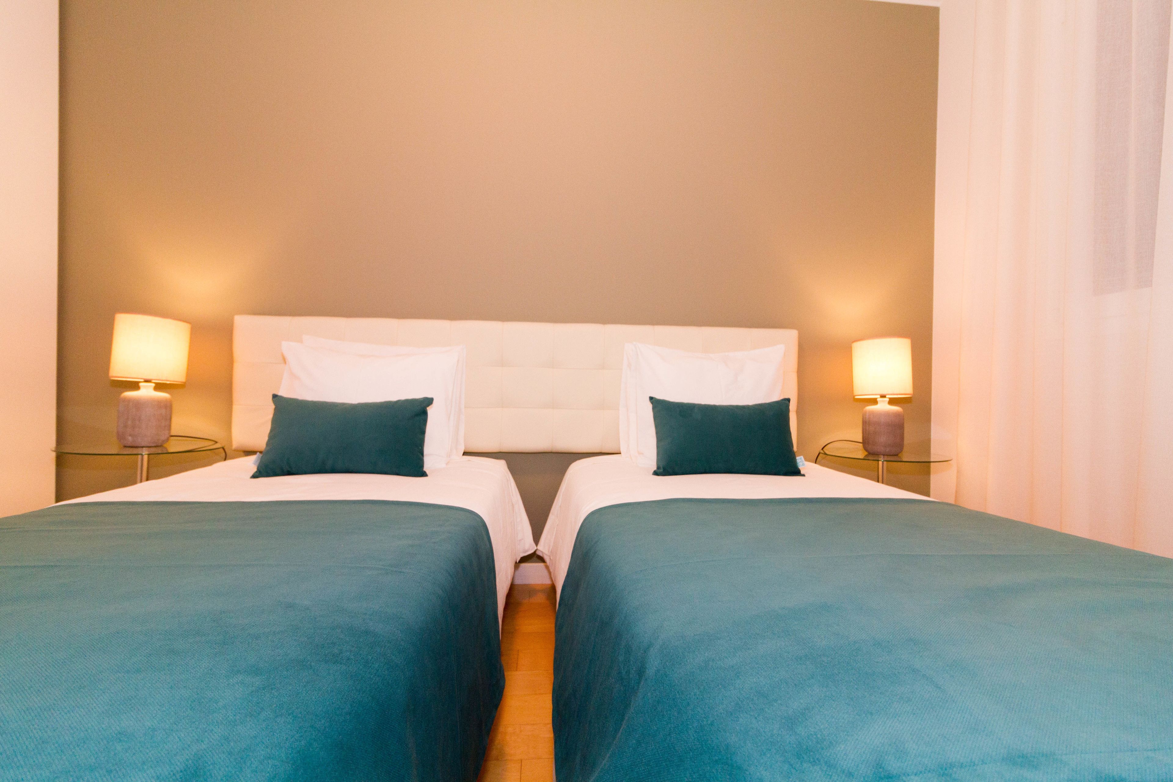 A double room with two beds, each with a pillow and a lamp on either side.