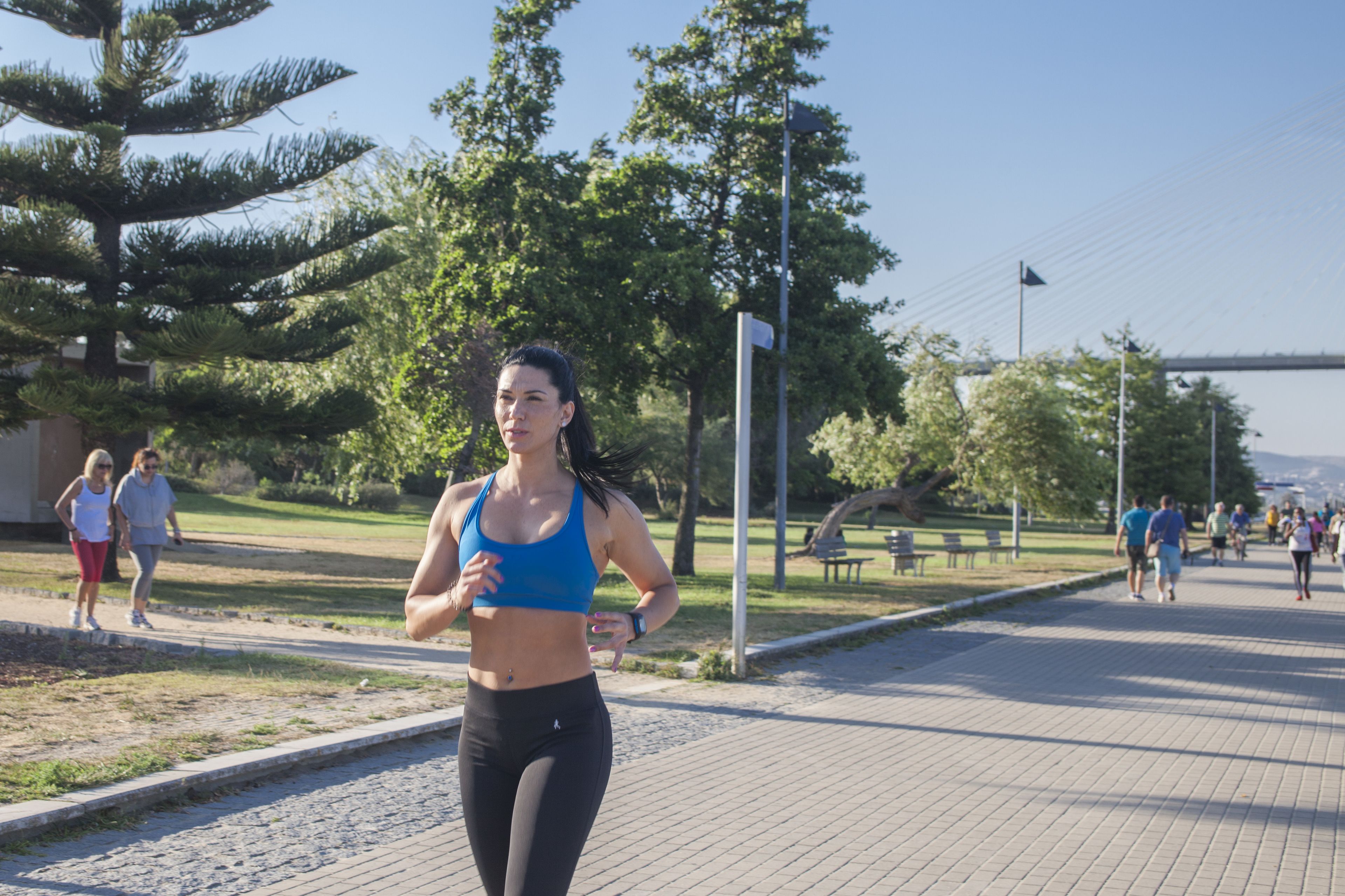Una mujer trotando por un sendero pavimentado en un parque con árboles y bancos.