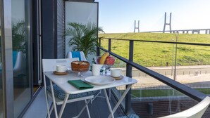 A balcony with a table set for breakfast, a view of a bridge, and a grassy area with a person walking a dog. - Oriente Rio Apartments by APT IIN - Parque das Nações (Lisbon)