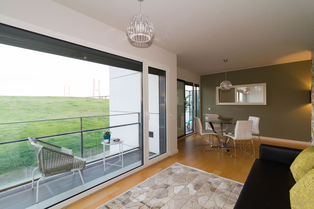 A modern living room with a balcony, a dining area, and a view of a bridge.