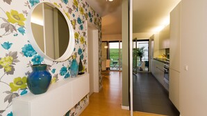 A hallway with a floral wallpaper, a round mirror, and a blue vase on a white console. - Oriente Rio Apartments by APT IIN - Parque das Nações (Lisbon)
