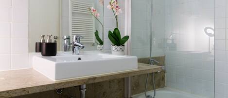 Ein Badezimmer mit einem weißen Waschbecken, einem Spiegel, einer Dusche und zwei Orchideen im Topf.