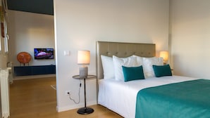 A hotel room with a bed, two bedside lamps, a TV on a stand, and a small table with a candle. - Oriente Rio Apartments by APT IIN - Parque das Nações (Lisbon)