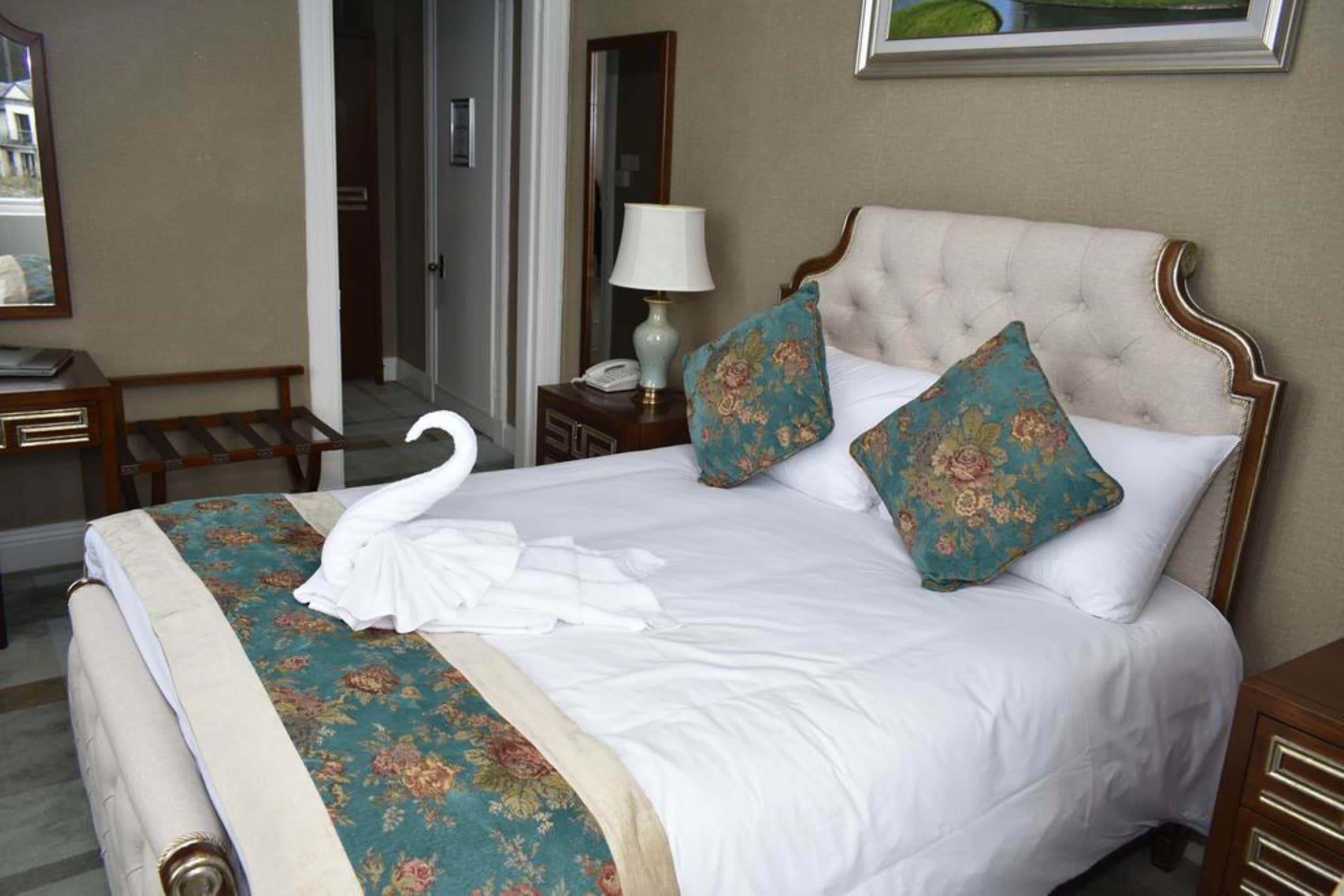 A neatly made bed with a floral bedspread, two decorative pillows, and a swan-shaped towel.