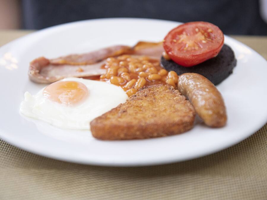 A plate of breakfast food including eggs, beans, sausages, and a tomato.