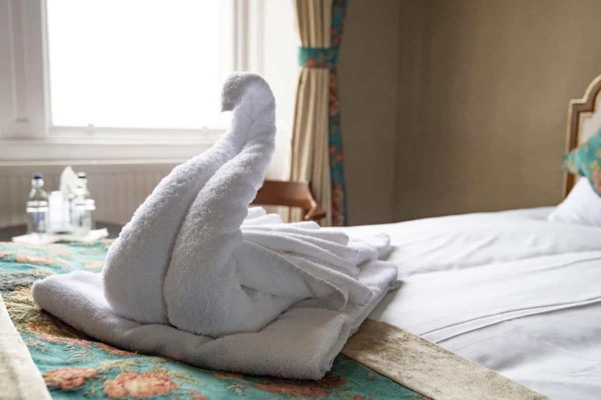 A neatly made bed with a floral-patterned bedspread and a stack of white towels on the side.