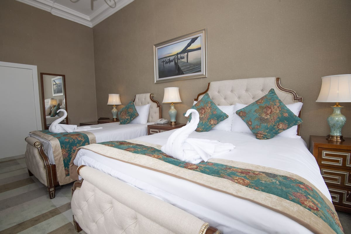 A hotel room with two beds, each with a swan-shaped towel, a large painting on the wall, and a mirror reflecting part of the room.