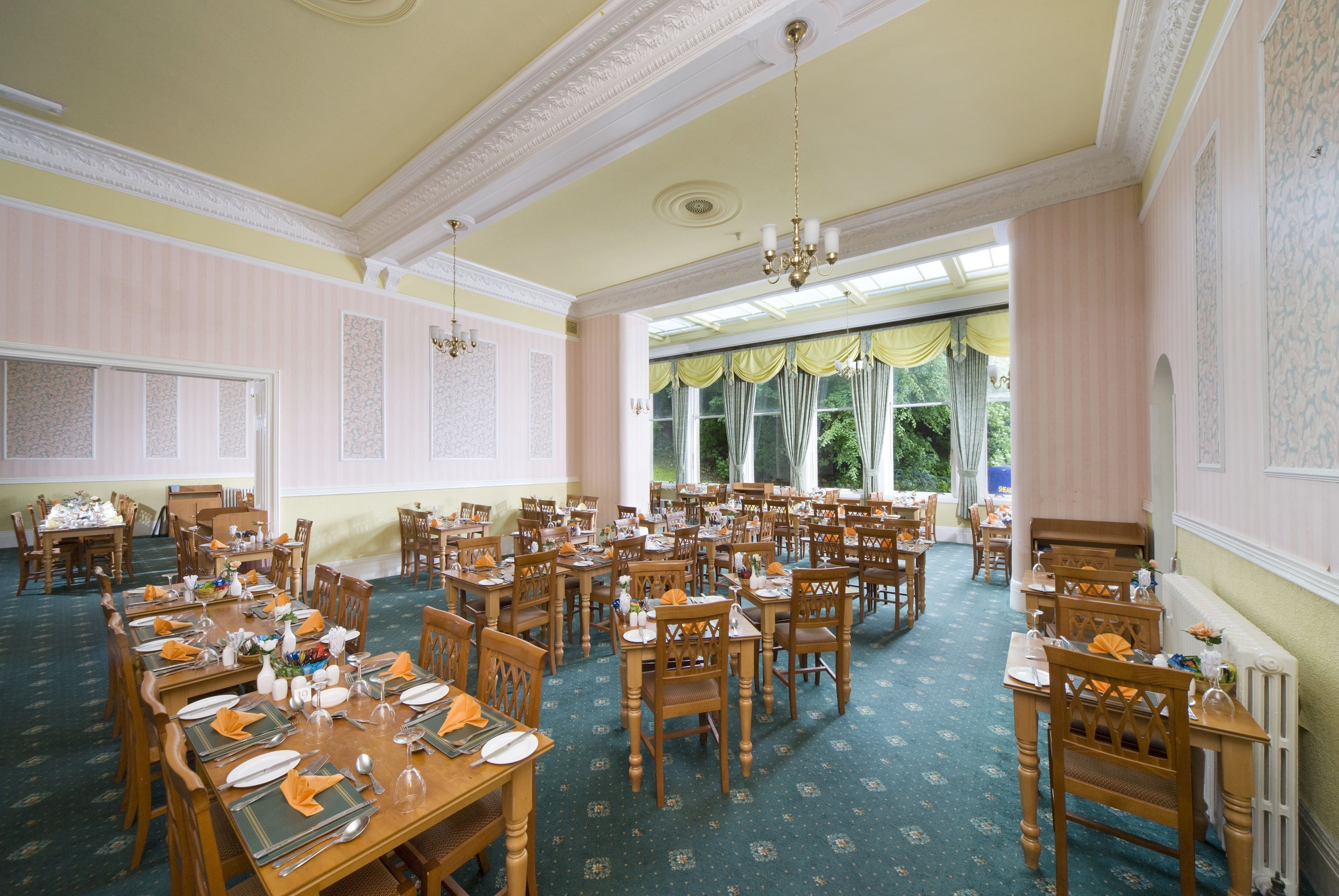 A large dining hall with multiple tables set for a meal, featuring classic wooden furniture and a green carpeted floor.