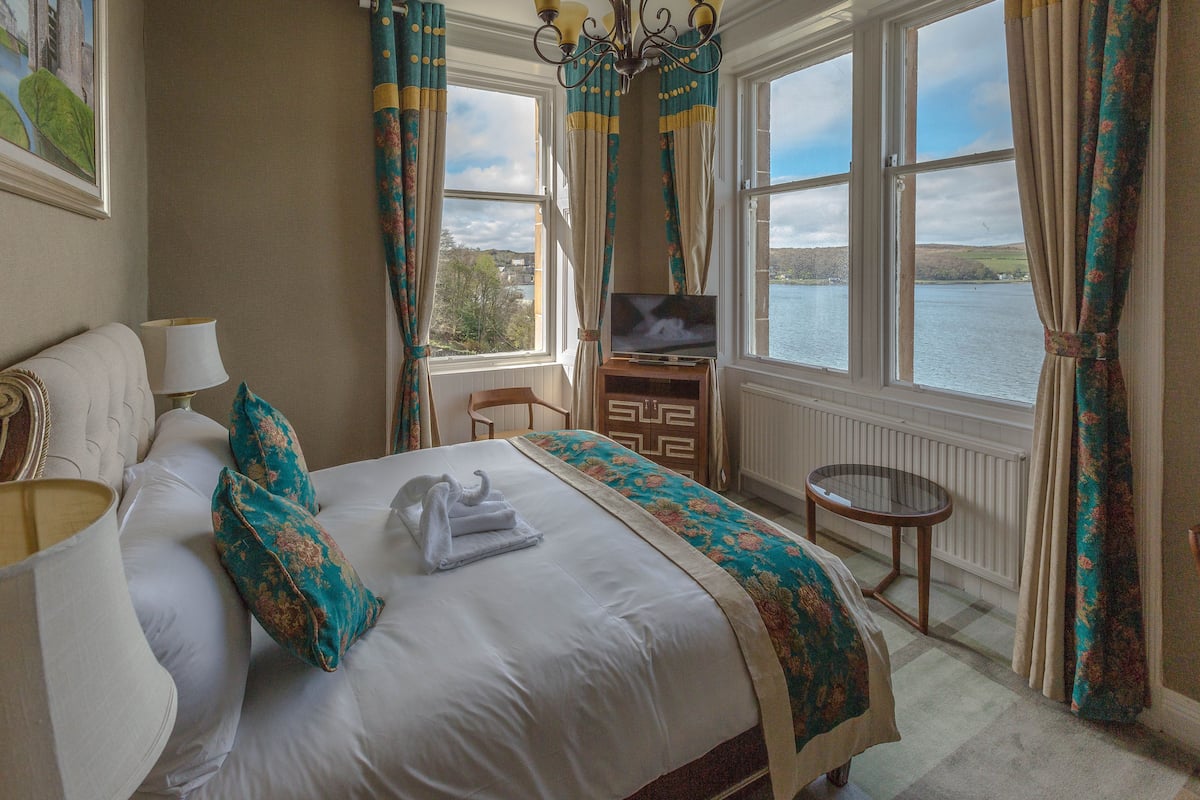 A hotel room with a bed, a TV, a chair, and a view of a lake.