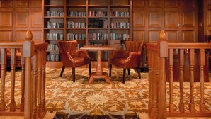 A library with bookshelves, a table, and leather chairs.