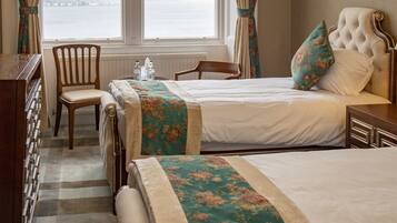 A hotel room with two beds, a view of the sea through a large window, a wooden dresser, and a chair.