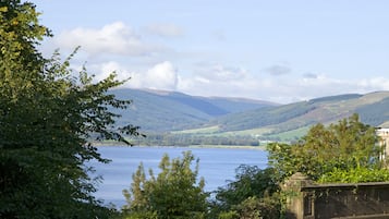 A scenic view of a lake with mountains in the background, a road with a stone wall, and lush greenery.