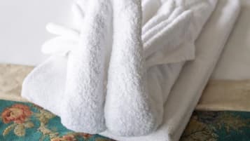 A neatly folded white towel on a bed with floral-patterned bedding and matching pillows.