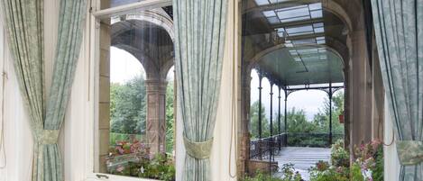 Un comedor con una mesa dispuesta para seis personas, ventanas grandes con cortinas y vistas a un jardín.