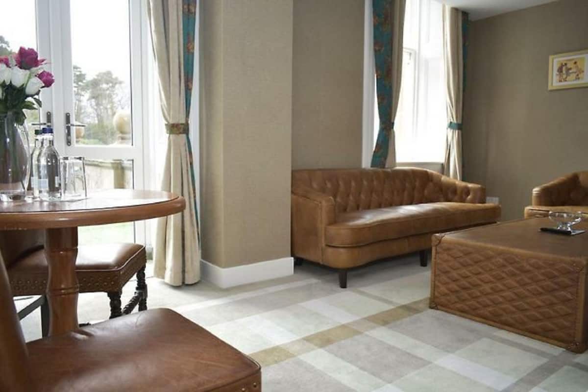 A living room with a brown leather sofa, a round wooden table with chairs, and a quilted ottoman.