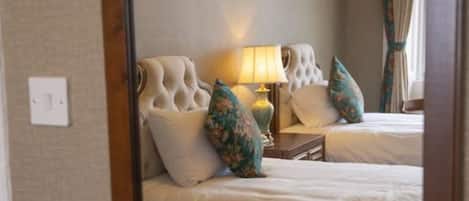 A hotel room with two beds, a framed picture on the wall, a lamp, and a window with curtains.