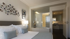 A modern hotel room with a large bed, a bedside table with a lamp, a wall-mounted abstract art piece, and a bathroom visible through an open door. - Oriente Marina Apartments by APT IIN - Parque das Nações (Lisbon)
