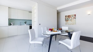 A modern kitchen with white cabinets and a dining area with a glass table and white chairs. - Oriente Marina Apartments by APT IIN - Parque das Nações (Lisbon)