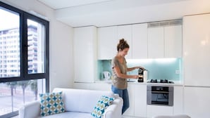 A modern kitchen with white cabinets, a coffee machine, and a sofa with patterned cushions. - Oriente Marina Apartments by APT IIN - Parque das Nações (Lisbon)