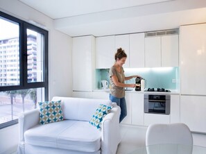 A modern kitchen with white cabinets, a coffee machine, and a sofa with patterned cushions. - Oriente Marina Apartments by APT IIN - Parque das Nações (Lisbon)