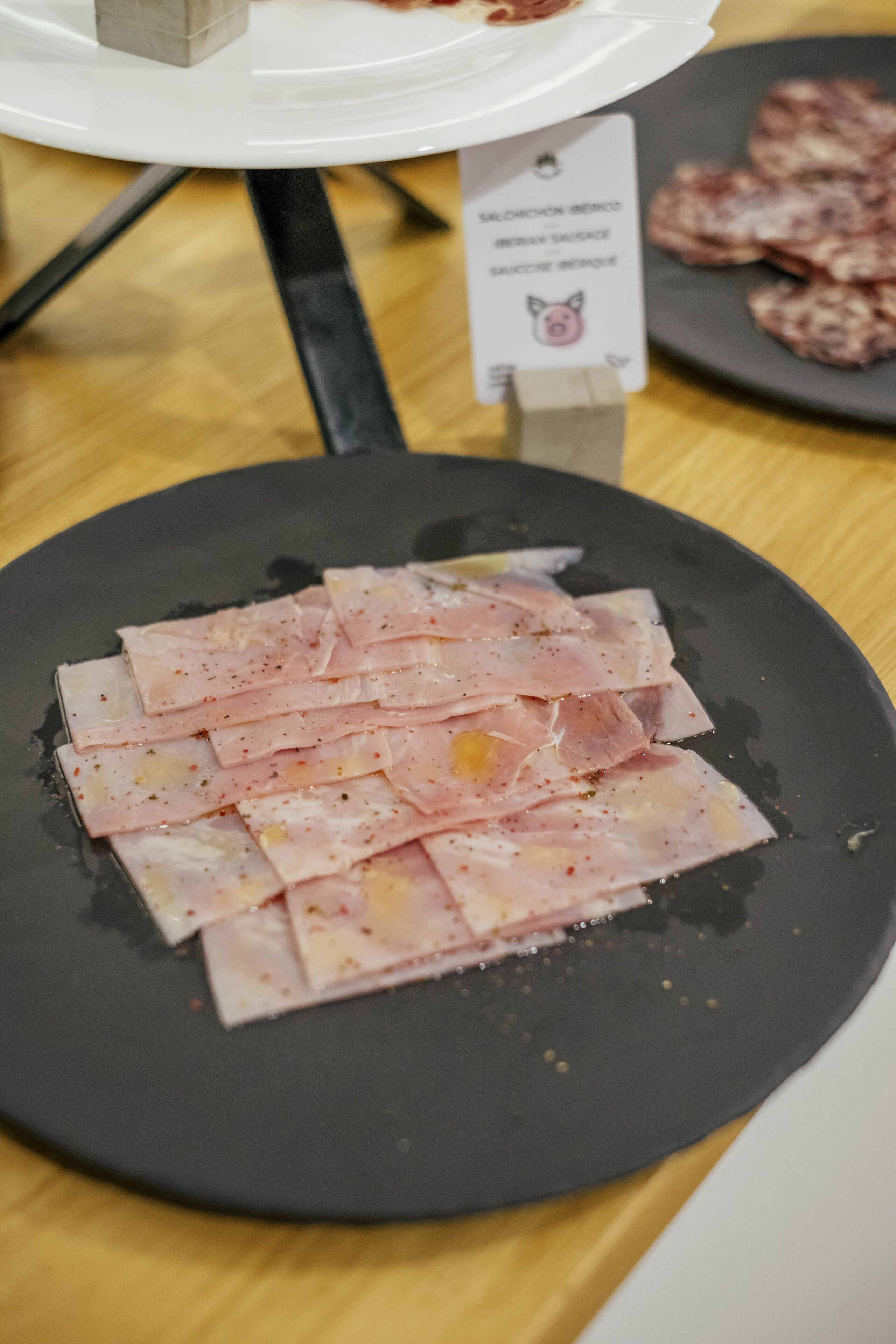 A black plate with sliced meat on a wooden table.