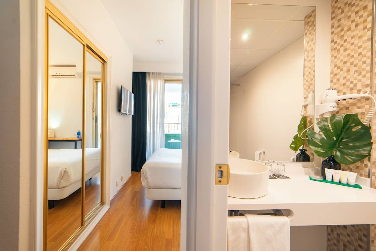 Une chambre d’hôtel avec un lit, une salle de bain comprenant un lavabo et un miroir, ainsi qu’un grand miroir qui reflète la pièce.