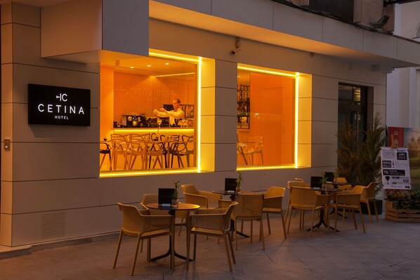 The exterior of the HC Cetina Hotel with outdoor seating and a bar area visible through the windows.
