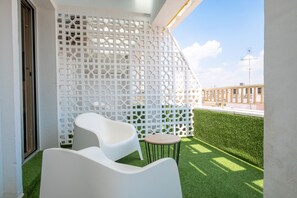 Un balcon avec des chaises blanches et une petite table, une cloison en treillis blanc, et une vue sur le paysage urbain.