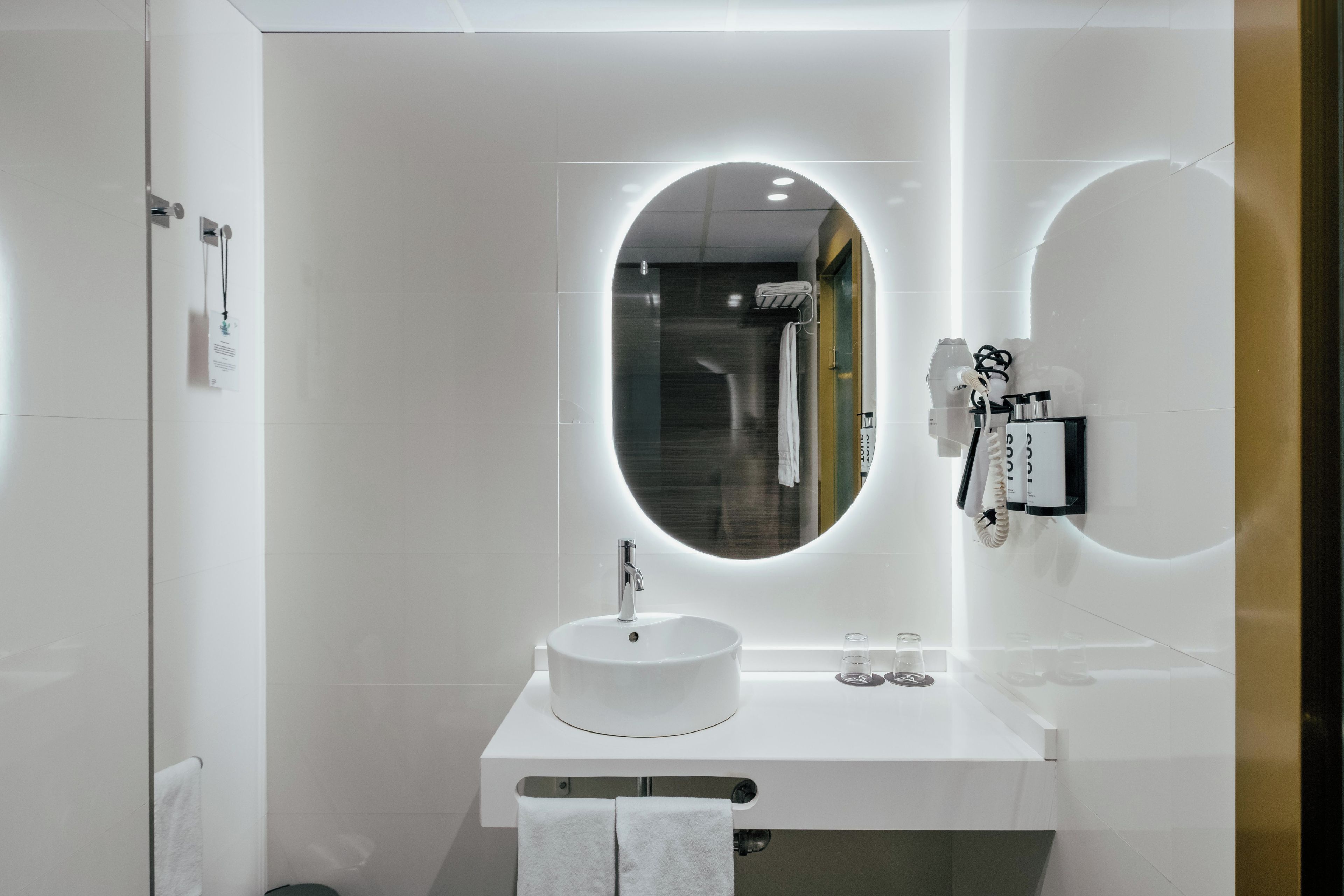 Une salle de bain moderne avec un miroir rond, un lavabo blanc et un porte-serviettes.