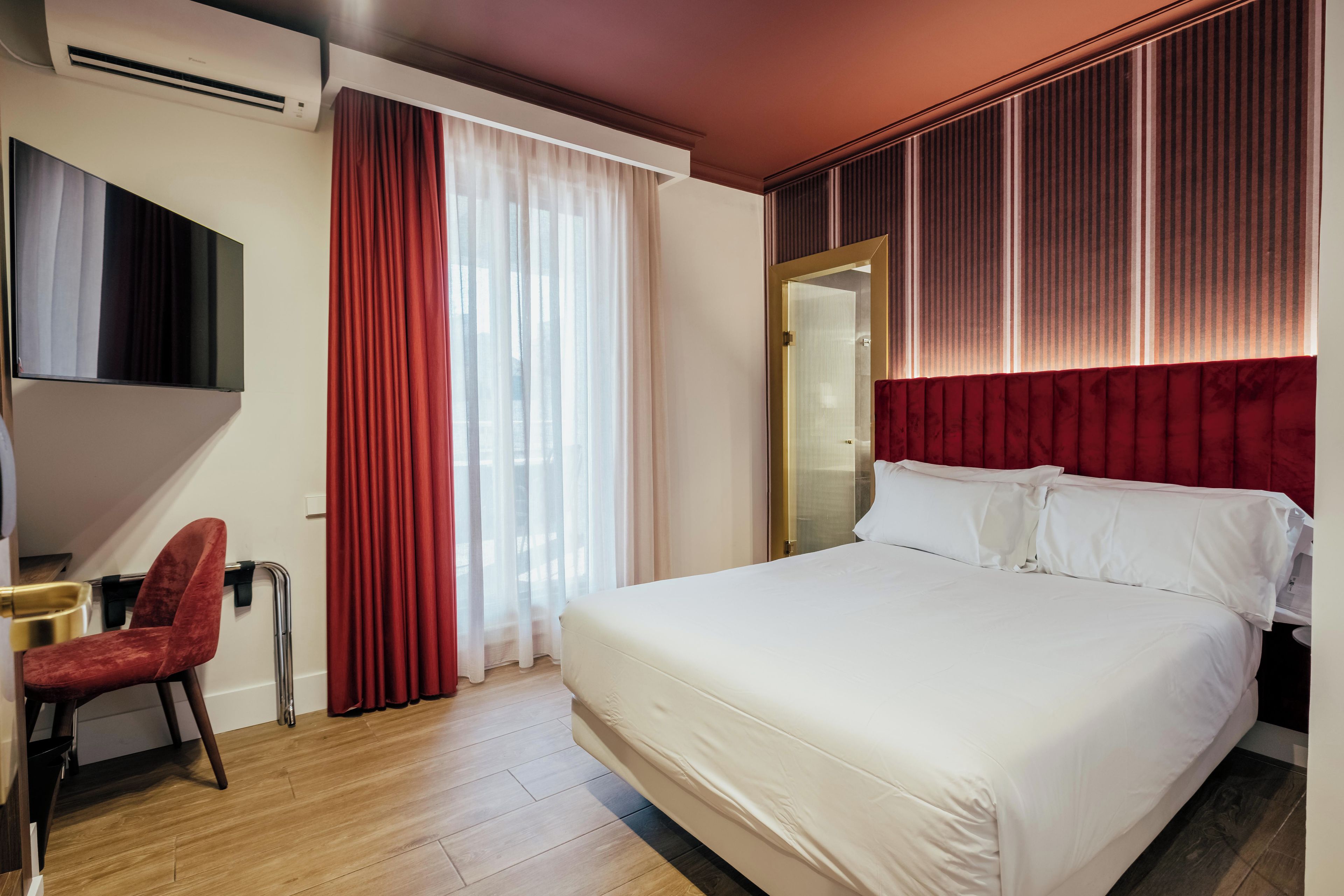 A hotel room with a bed, a desk, a chair, a TV, and a window with curtains.