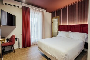A hotel room with a bed, a desk, a chair, a TV, and a window with curtains.